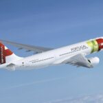 A TAP Air Portugal jet flying upwards in front of a cloudy sky.