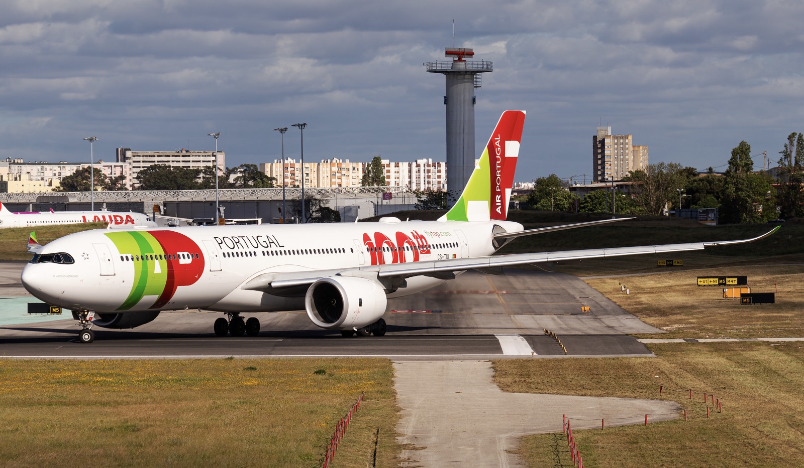 A red, white, and green TAP Air Portugal jet on the runway at Humberto Delgado Airport, Lisbon (LIS).