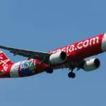 A red and white Thai AirAsia Airbus A321neo flying upwards in front of a clear blue sky.