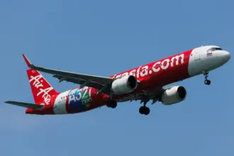 A red and white Thai AirAsia Airbus A321neo flying upwards in front of a clear blue sky.