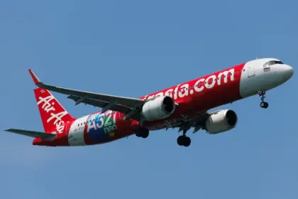 A red and white Thai AirAsia Airbus A321neo flying upwards in front of a clear blue sky.