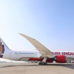 A red and white Air India Boeing 787-9 sat on a runway in front of a clear blue sky on a sunny day.