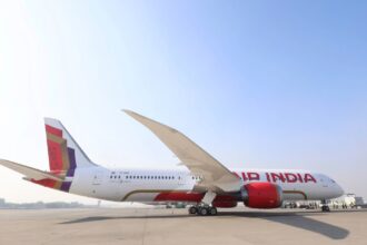 A red and white Air India Boeing 787-9 sat on a runway in front of a clear blue sky on a sunny day.