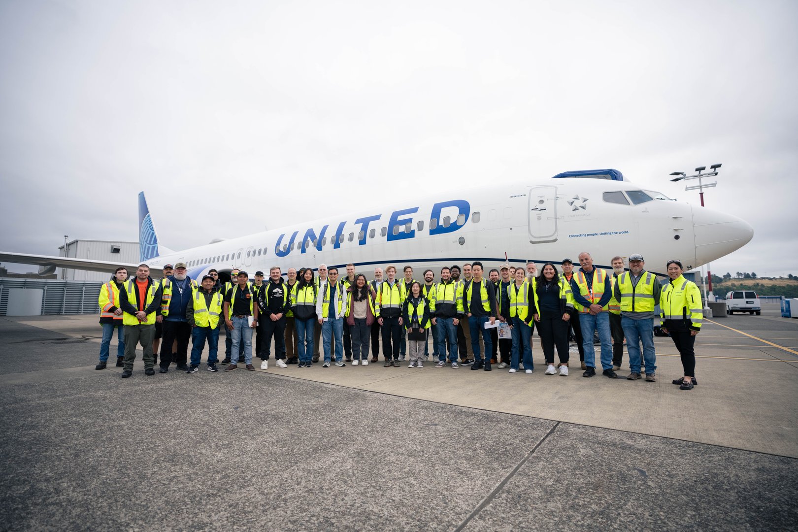 A team of ground crew in hi-vis jackets stood on a runway in front of a Boeing 737 Max 10 jet, painted with the logo of United Airlines.