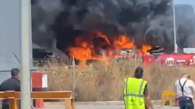 The large fire from a distance, vehicles are ablaze and people look towards the fire and explosions