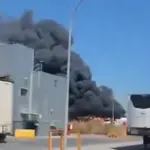 Smoke is seen billowing across Mallorca airport behind a building. Lorries pass on the road in front.