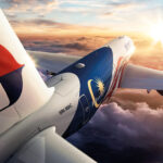 An aircraft flying into a golden sunset, with fluffy clouds below.