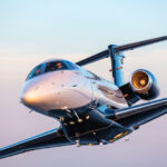 Embraer Phenom 300EV in flight at sunset, close-up view of the nose, cockpit and right engine.
