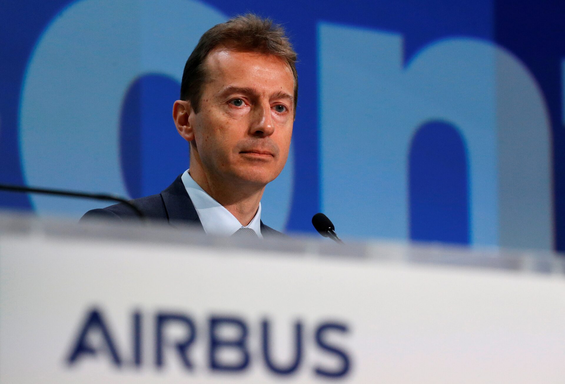 Airbus CEO Guillaume Faury standing at a microphone wearing a black suit with Airbus logos on the microphone stand.