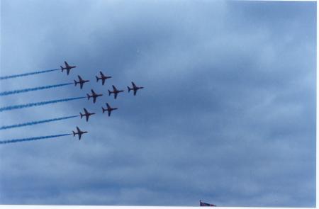 Image shows nine Red Arrows aircraft flying in formation at the Farnborough Airshow in 2004 in a cloudy blue sky