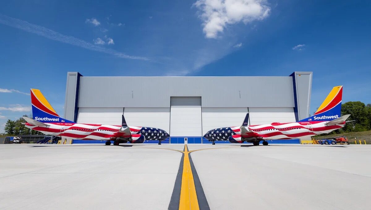 Two aircraft facing each other, with the American flag design across the fuselage. With yellow, red and blue on the tail with "Southwest" written in white. A grey building in the background, with blue sky.