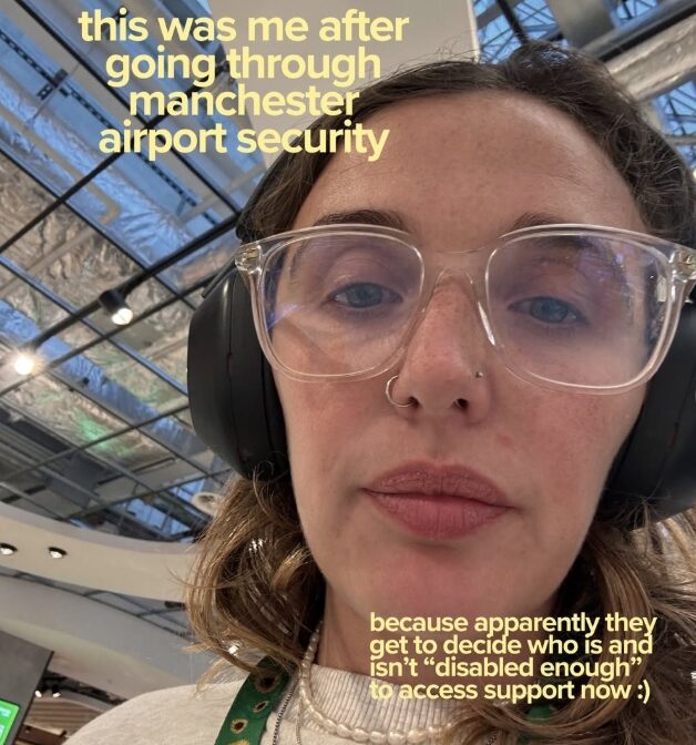 A selfie of Ellie Middleton, a Caucasian presenting woman with light brown hair wearing large black overhead headphones, glasses with clear frames, and a sunflower lanyard over her white-cream jumper. She looks to have been crying. A caption on the top left of the image reads 'this was me after going through Manchester Airport security' and a caption in the bottom right reads 'because apparently they get to decide who is and isn't "disabled enough" to access support now :)', both ion light yellow writing. The image is taken from Ellie Middleton's Instagram page. 