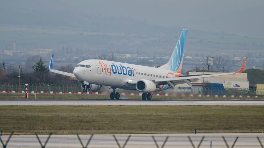 A Flydubai Boeing 737 plane landing on tarmac surrounded by green grass.