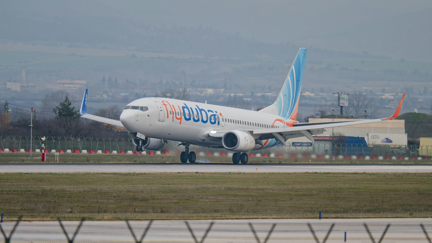 A Flydubai Boeing 737 plane landing on tarmac surrounded by green grass.