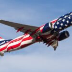 A Southwest Airlines aircraft flying in the blue, cloudy sky, toward the right side. New America250 livery.