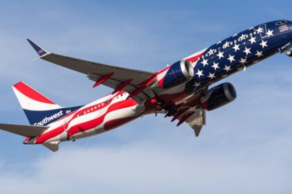 A Southwest Airlines aircraft flying in the blue, cloudy sky, toward the right side. New America250 livery.