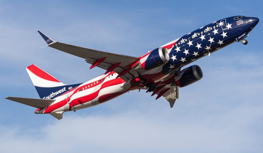 A Southwest Airlines aircraft flying in the blue, cloudy sky, toward the right side. New America250 livery.