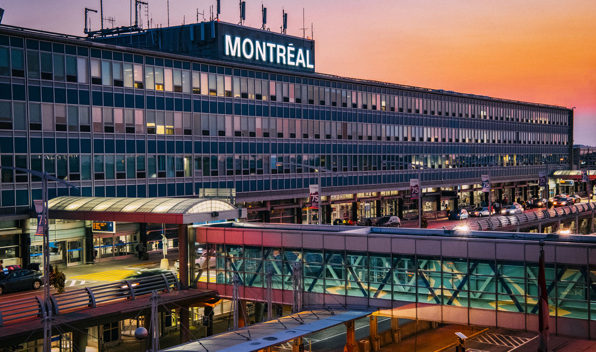 YUL airport outside with Montreal sign and skybridge at sunset. Cars are pulling up to the pick up and drop off point.