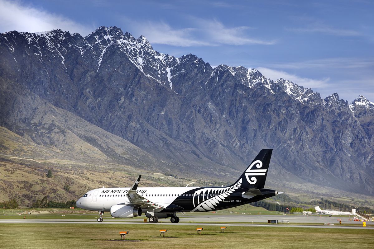 Aeroplane on runway with mountains in background covered in snow at the top, and a blue sky