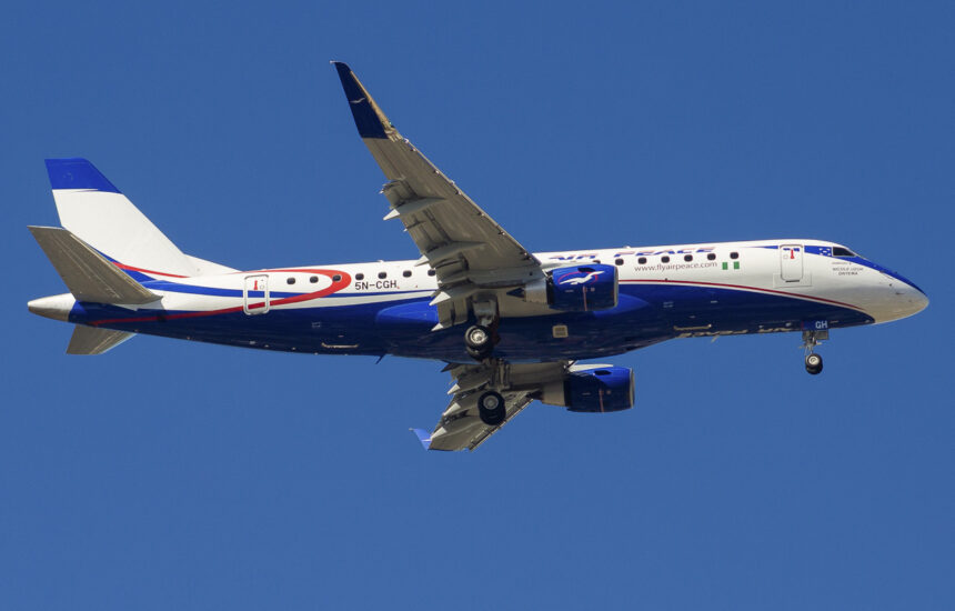 An Air Peace plane mid-flight, showing the bottom of the plane's fuselage and underside of its wings.