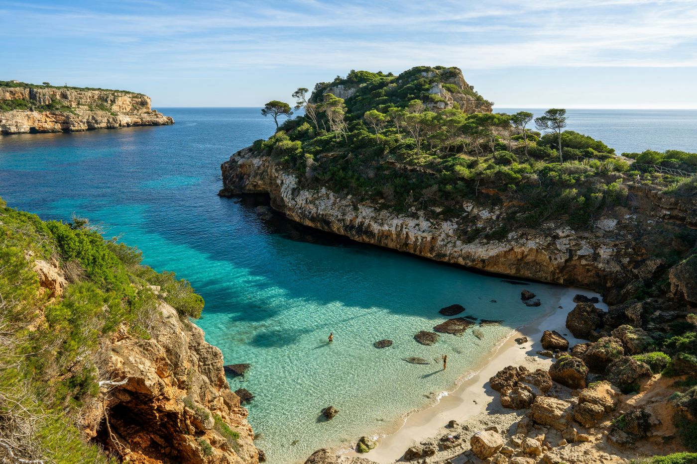 A sky view of a sandy mallorca beach with cliffs, crystal blue water, and palm trees