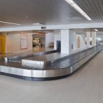 An empty airport baggage carousel can be seen in the middle of an empty airport terminal.