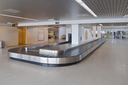 An empty airport baggage carousel can be seen in the middle of an empty airport terminal.
