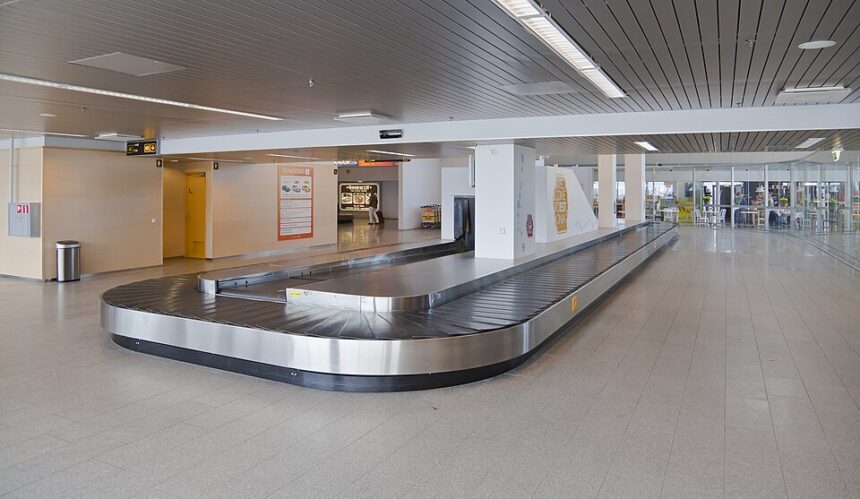 An empty airport baggage carousel can be seen in the middle of an empty airport terminal.