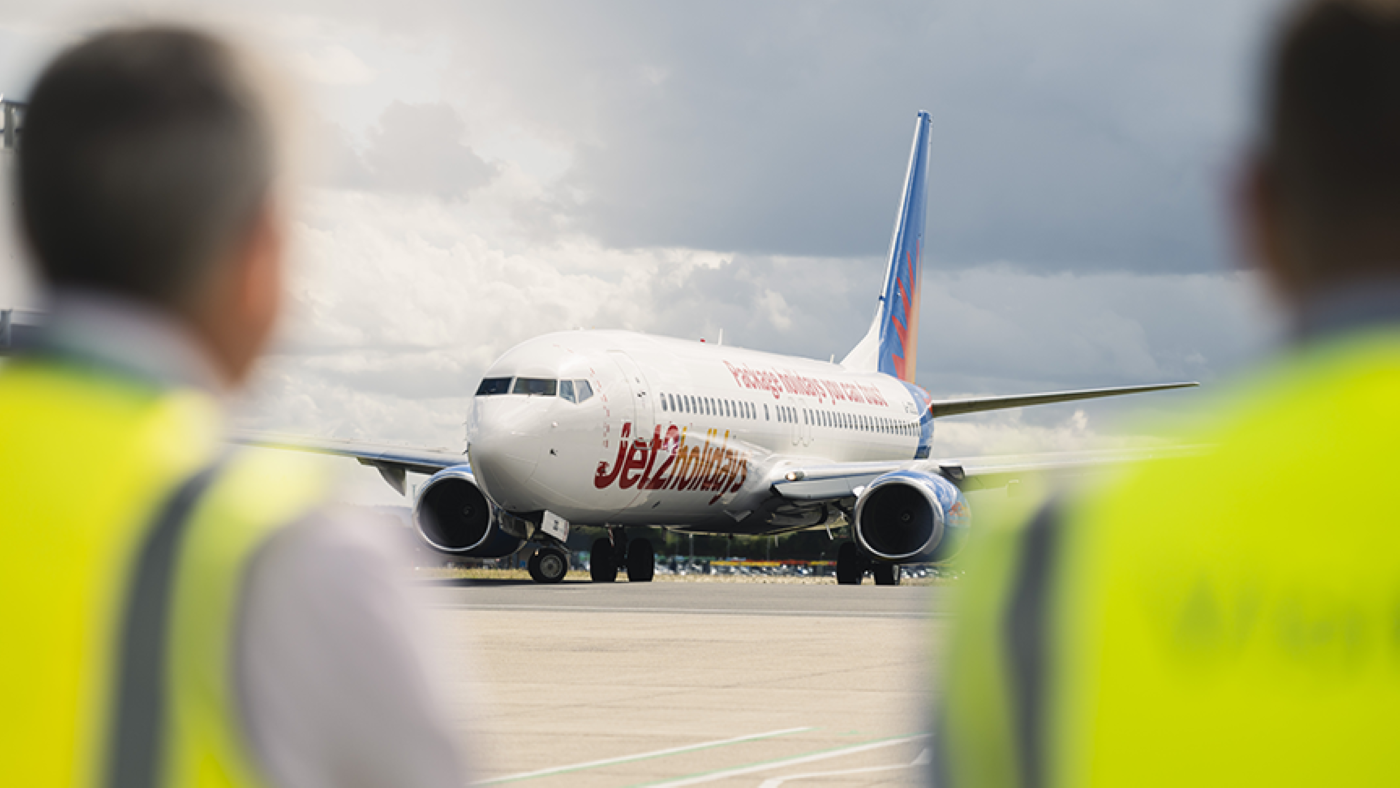 Bristol Airport staff in high visibility jackets standing on tarmac with a grounded aircraft in the background