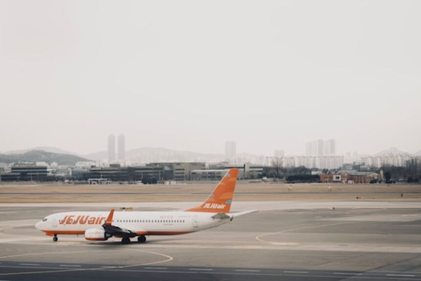 A Jejuair Boeing 737-800 parked at the Gimpo International Airport tarmac with a cloudy sky backdrop and hills in the horizon