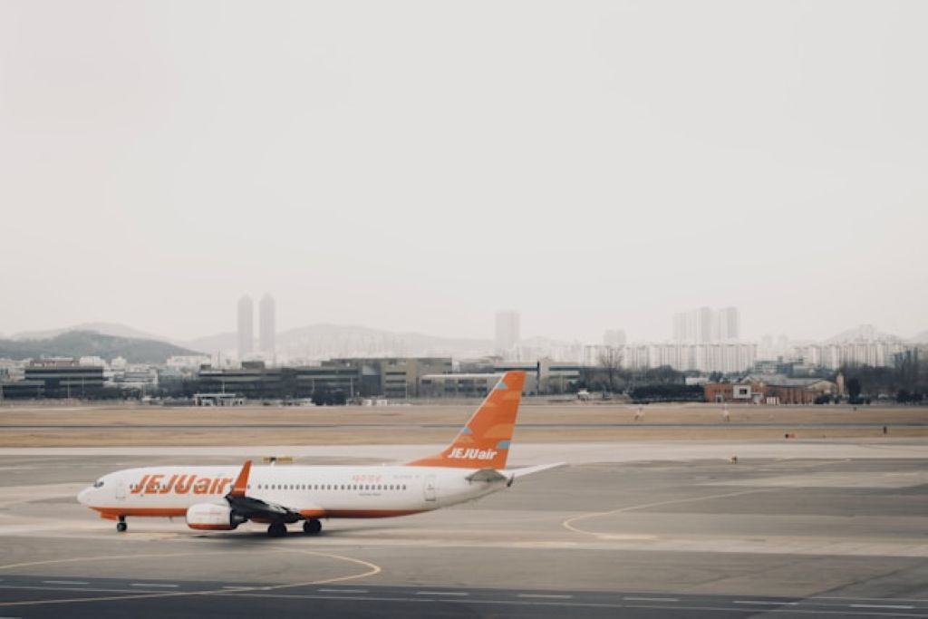 A Jejuair Boeing 737-800 parked at the Gimpo International Airport tarmac with a cloudy sky backdrop and hills in the horizon