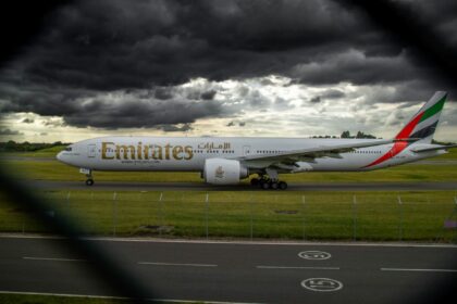 A side view of an Emirates aircraft on the Birmingham Airport tarmac with grass surrounding it and a dark cloudy sky.