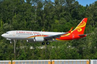 A Hainan Airlines Boeing 737 aircraft preparing to land on tarmac with trees in the background.
