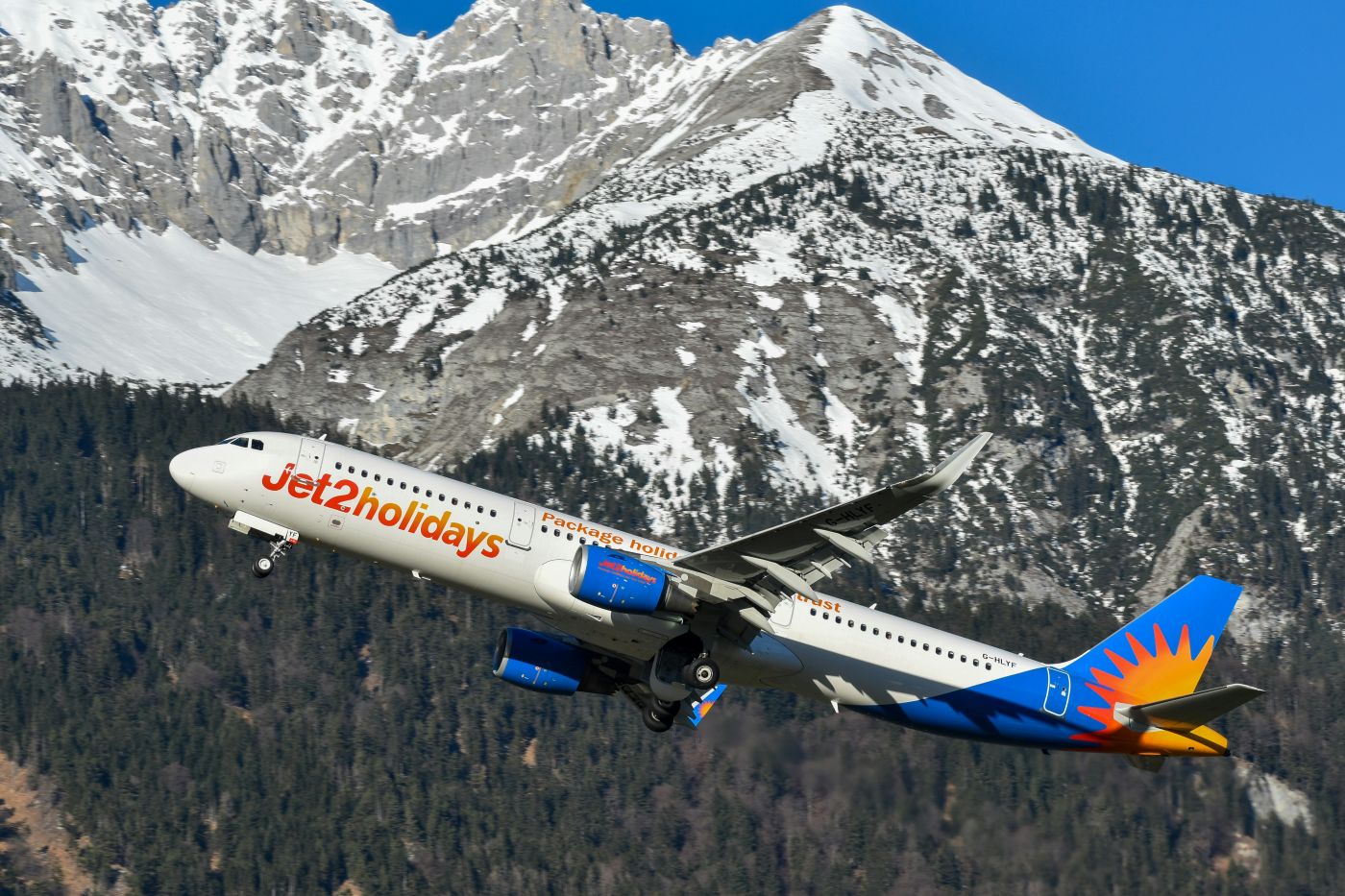 Jet2 aircraft maneuvering among snow topped mountains with a clear blue sky backdrop
