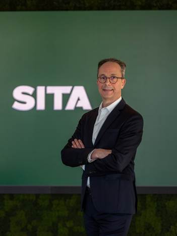 Image shows CEO of SITA David Lavorel in the foreground with his arms crossed and behind him a white SITA logo