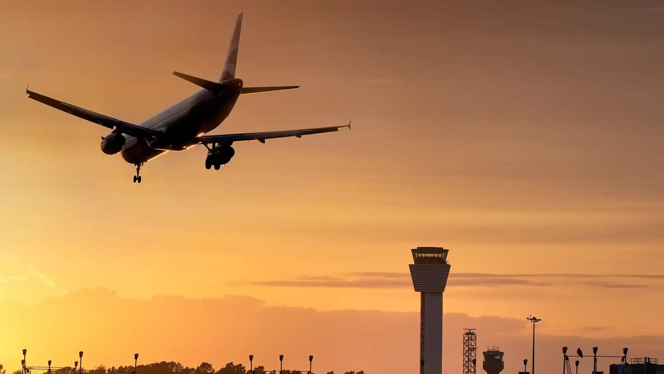 Plane landing over Dublin Airport air traffic control tower, orange and yellow sunset in the background.