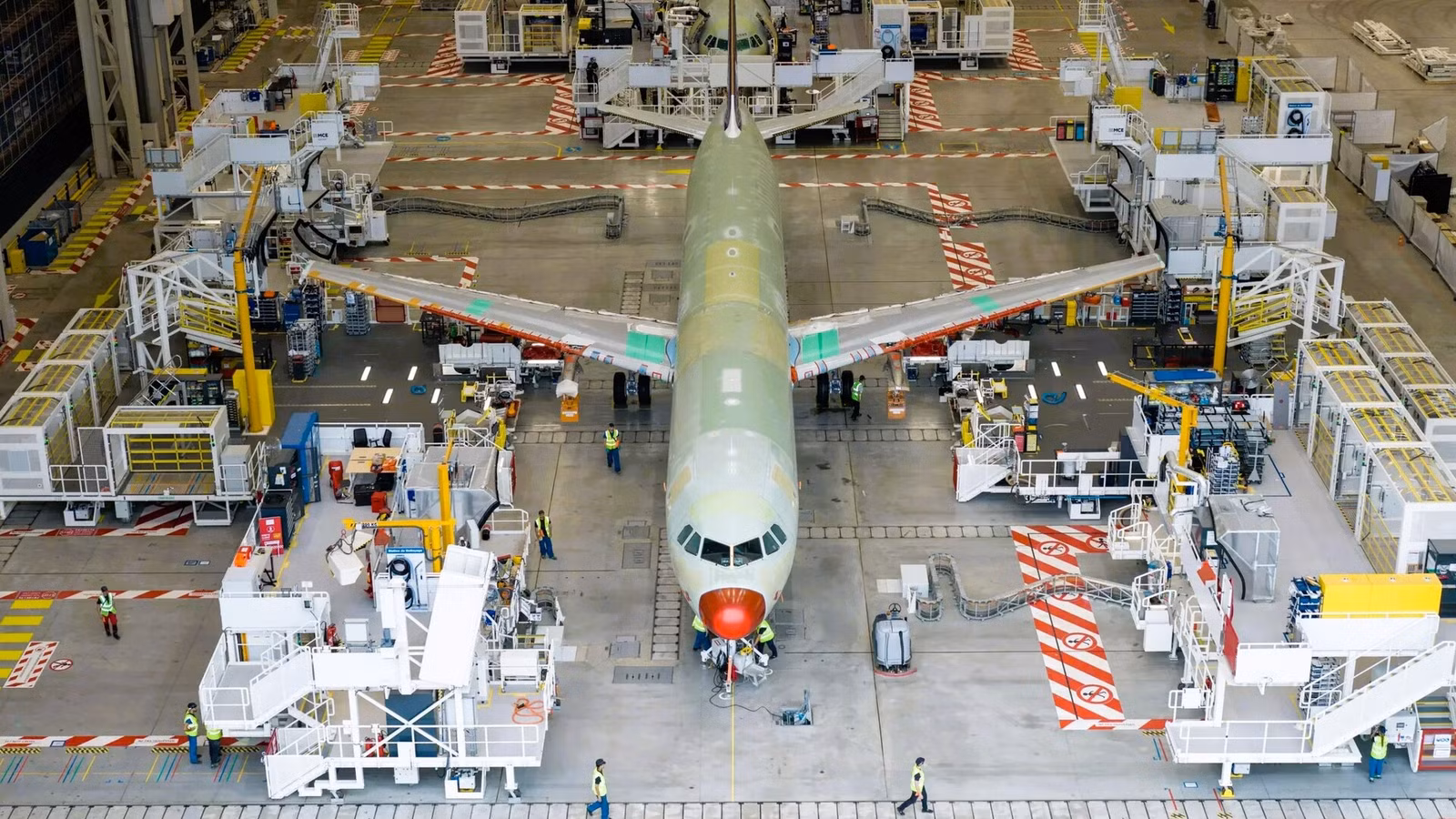 Inside the Airbus factory birds eye view with many people working on an aircraft shell. Machines are around the aircraft and there is another aircraft behind also being worked on.