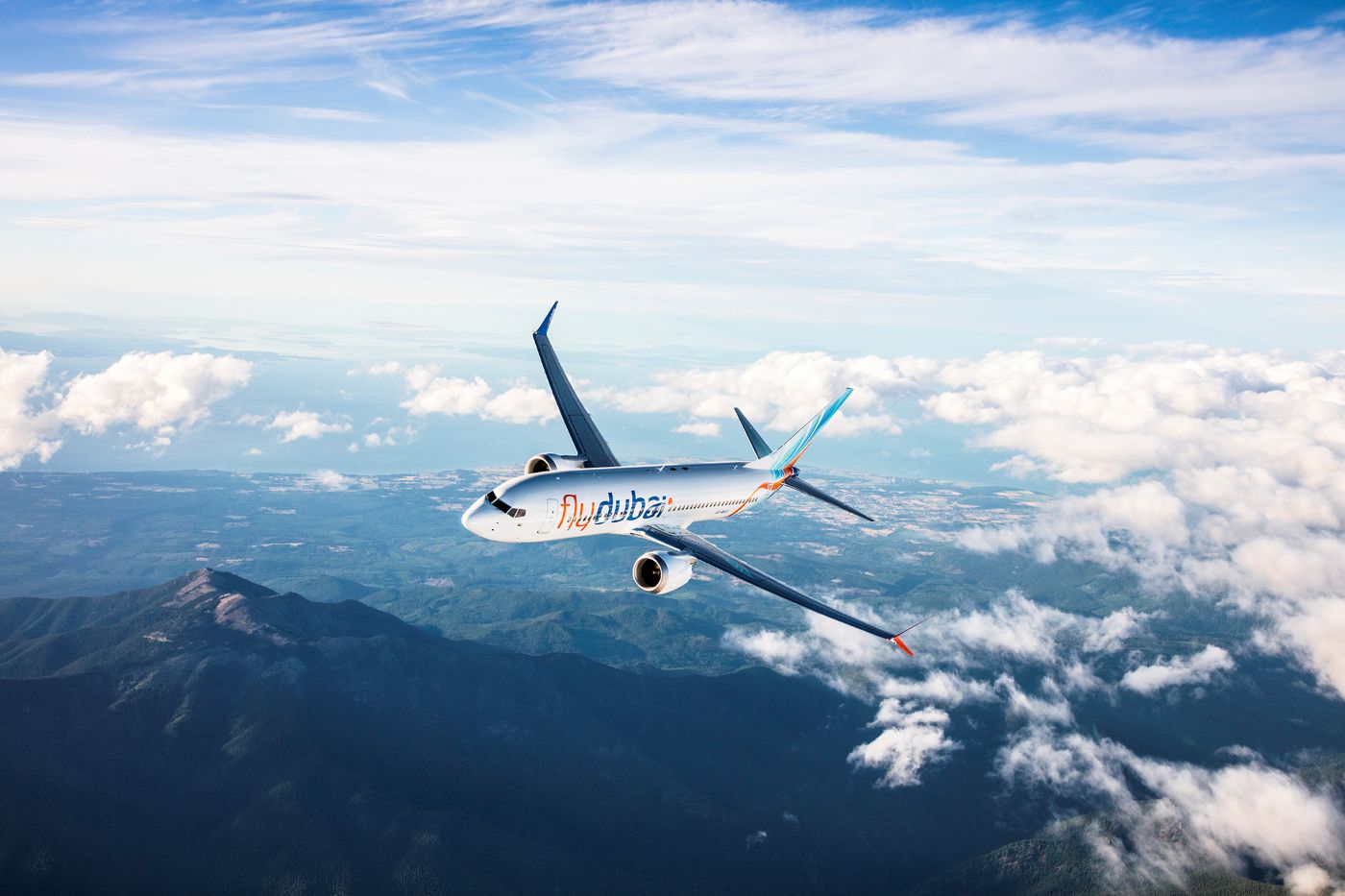 A Flydubai Boeing 737 MAX 8 plane maneuvering midair over a mountain and a clear sky