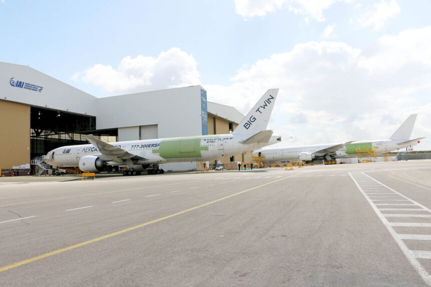 Two Boeing 777-300ERSF converted freighter aircraft, in Kalitta Air and AerCap Cargo liveries, parked outside an IAI Aviation Group hangar.