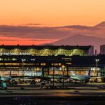 HND entrance at sunset with a mountain in the background. cars are parked in front of the building which has lots of lights.
