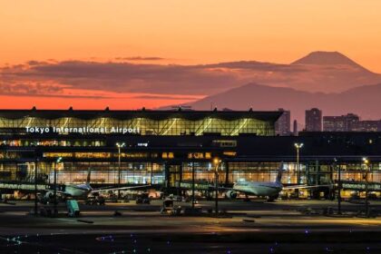 HND entrance at sunset with a mountain in the background. cars are parked in front of the building which has lots of lights.
