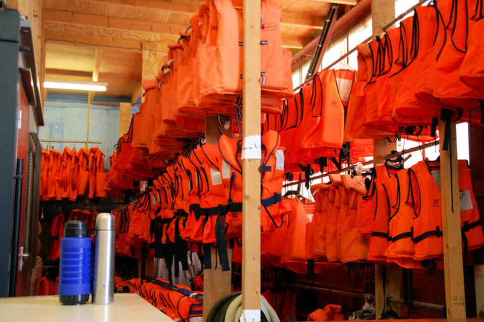 Rows of orange life jackets hung up on wooden posts.