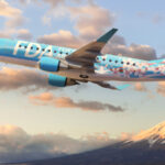 An image of an FDA aircraft flying with a snowy mountain top and clouds in the background.