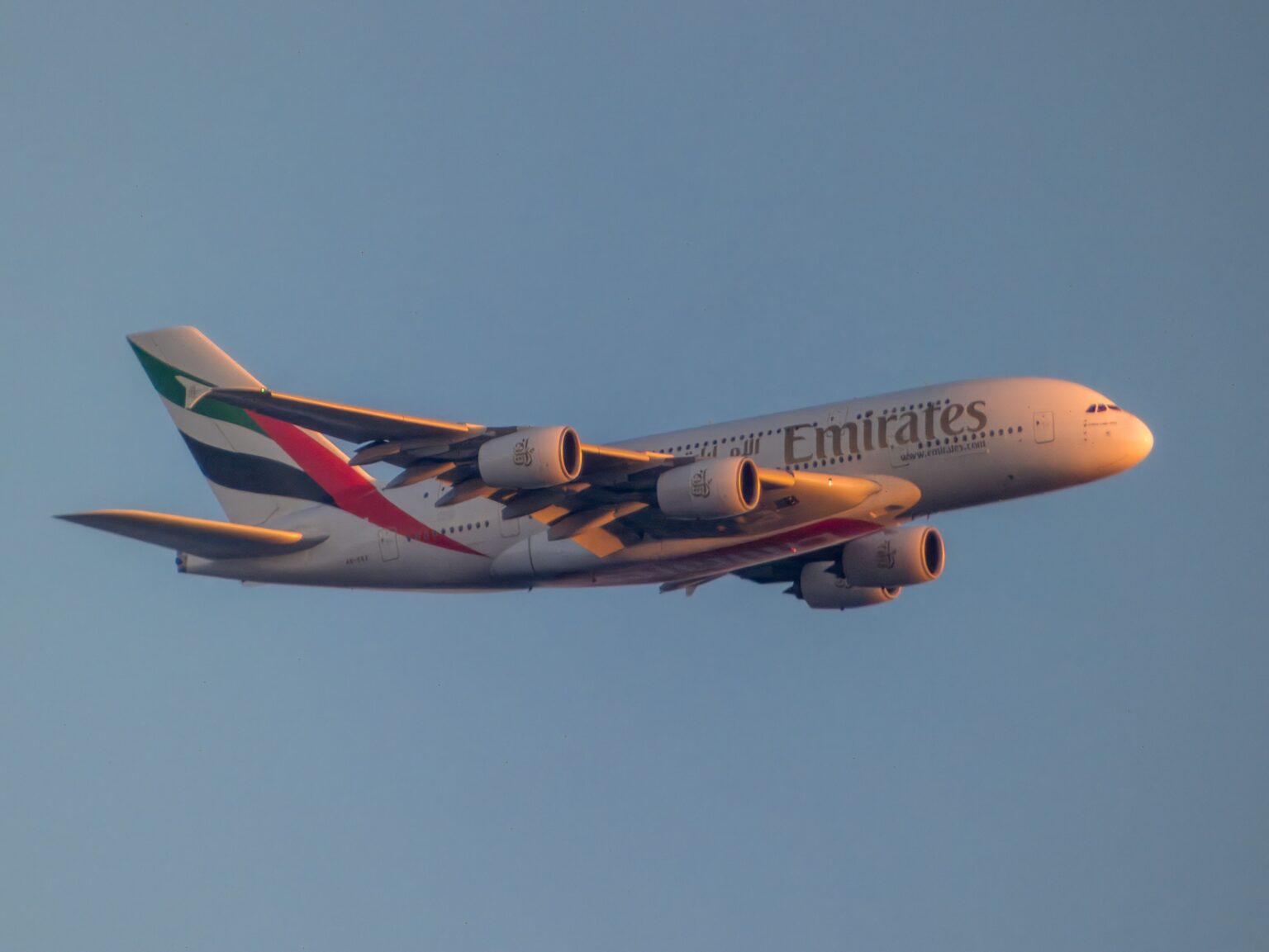 An Emirates Airbus A380 flying against a clear blue sky, with the airline’s logo and distinctive UAE flag colours visible on the aircraft