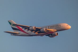 An Emirates Airbus A380 flying against a clear blue sky, with the airline’s logo and distinctive UAE flag colours visible on the aircraft