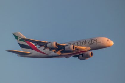 An Emirates Airbus A380 flying against a clear blue sky, with the airline’s logo and distinctive UAE flag colours visible on the aircraft