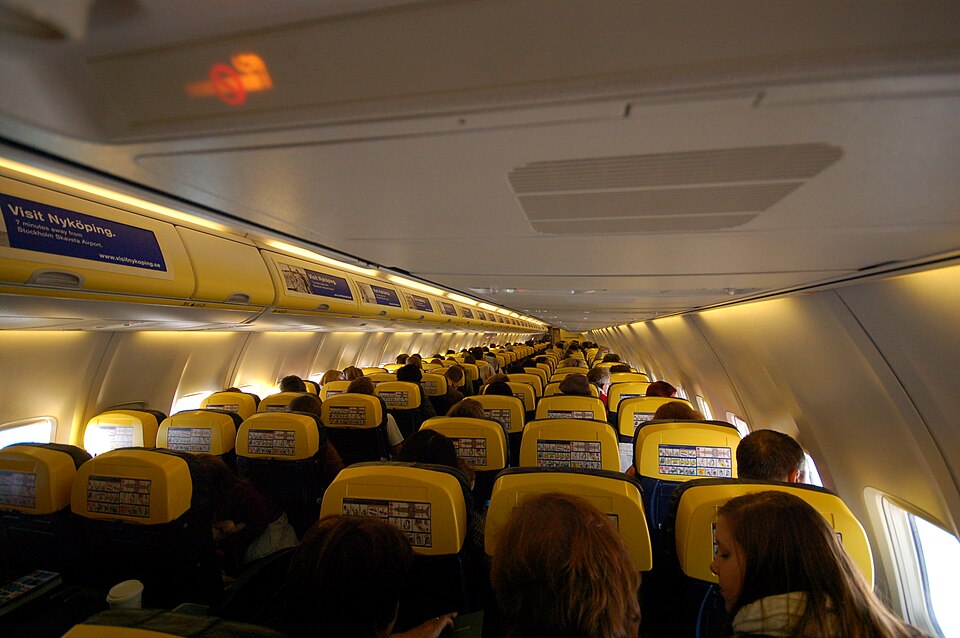 The interior of a Ryanair Boeing 737 showing the backs of several rows of seats and yellow overhead storage lockers. 