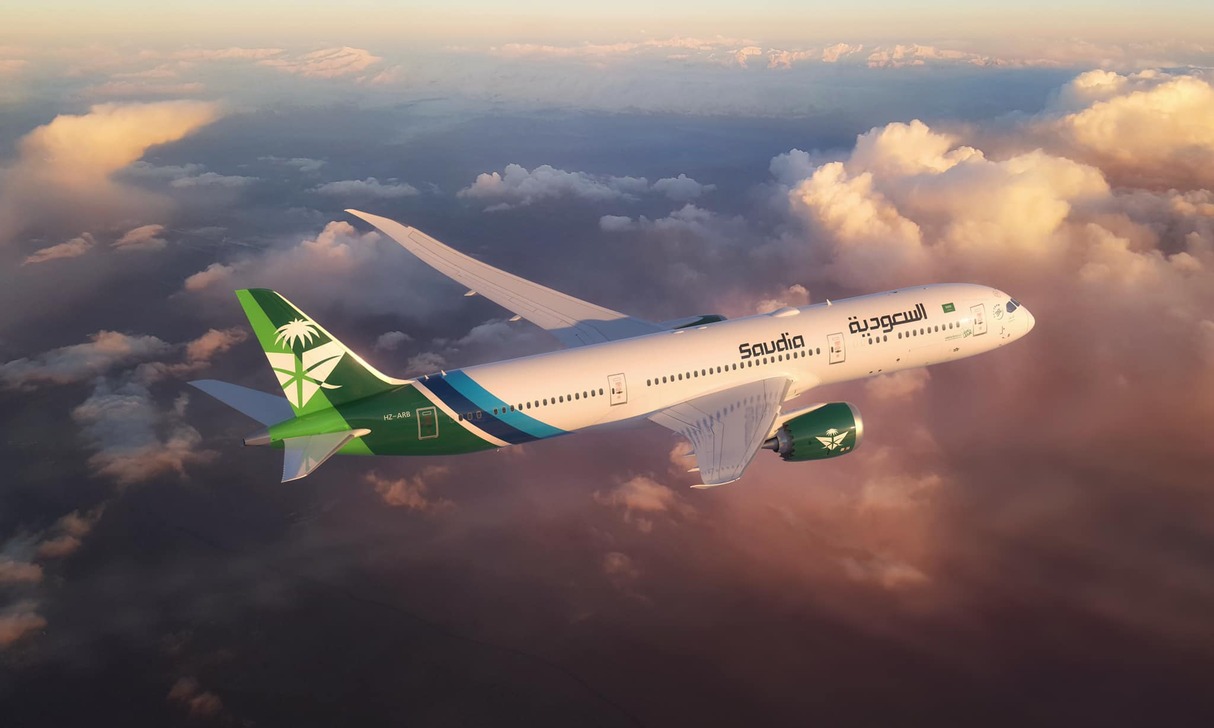 The exterior of a Saudia aircraft cruising at altitude above the clouds.