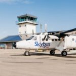A white Skybus aircraft on the tarmac at an airport. Blue sky in the background.