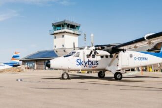 A white Skybus aircraft on the tarmac at an airport. Blue sky in the background.